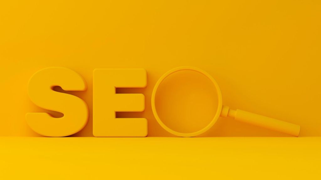 Grafika przedstawiająca napis "SEO" na żółtym tle. Litera "O" jest zastąpiona przez szkło powiększające.